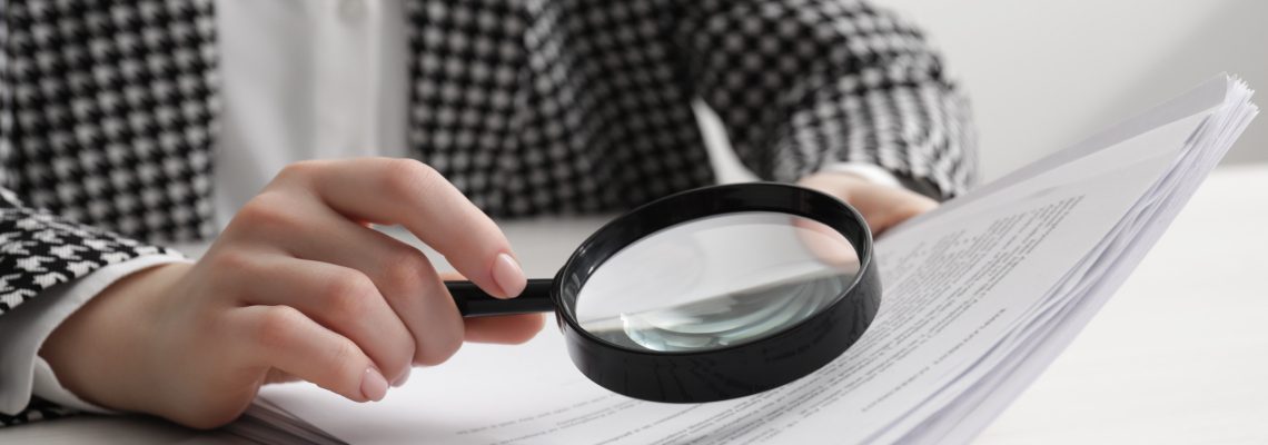 Woman looking at document through magnifier at white wooden table